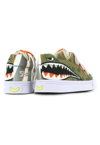 Groene canvas sneakers met een haai ontwerp, witte rubberen zool, oranje accenten en een gele glimlachdetail op de hiel.