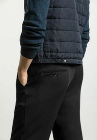 Vadderad väst i mörk marinblå färg med en texturerad ulltröja under, kompletterad med svarta byxor med en bakficka med knappstängning.