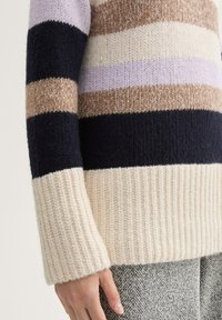 Sweter w paski ma naprzemienne pasy w kolorze granatowym, kremowym, jasnofioletowym, beżowym i brązowym. Wykonany z miękkiego dzianiny, z prążkowanymi mankietami i dołem.