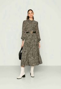 Vestido midi de mangas longas, com padrão animal em preto e bege, com um cós ajustado, complementado por um cinto preto e botas de cano curto brancas com salto.