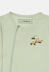 Φωτεινό πράσινο φορμάκι με φερμουάρ, κατασκευασμένο από μαλακό ύφασμα, που διαθέτει μια μικρή εκτύπωση με κατασκευαστικό όχημα σε κίτρινο και μαύρο χρώμα στο μπροστινό μέρος.