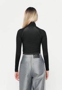 Musta pitkähihainen lyhyt toppi, jossa on korkea kaulus, yhdistettynä vaaleanharmaisiin korkeavyötäröisiin farkkusiin, joissa on logotägi ja sivunauhat.