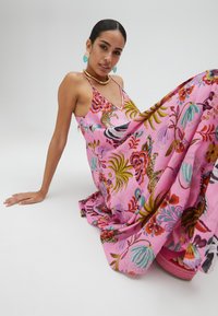 Robe maxi rose à motifs floraux vifs de feuilles et d'animaux. Dispose d'un décolleté en V et de bretelles spaghetti, fabriquée en tissu léger.