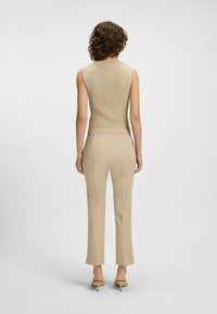 Beige ribbed ärmelloses Oberteil, kombiniert mit eng anliegenden beigen Hosen; schlanker Schnitt, strukturierter Stoff und dezente vertikale Streifen, abgerundet mit beigen Absatzschuhen.