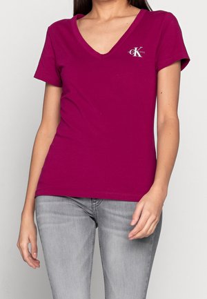 V-neck t-shirt in fuchsia cotton, short sleeves, features a small logo on the left chest, paired with light gray jeans.