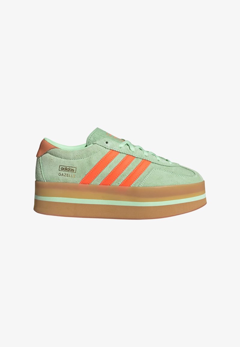 Zielone zamszowe sneakersy z pomarańczowymi paskami. Posiadają grubą, jasnobrązową platformę oraz tłoczone zdobienia na języku. Sznurówki są w pasującym zielonym kolorze.