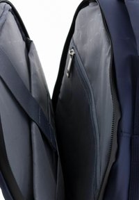 Navy backpack interior showing two compartments with smooth gray fabric, one featuring a zippered pocket. Textured exterior fabric is visible.