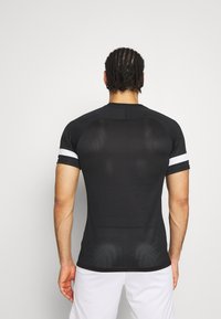 Camisa atlética negra de mangas cortas, con franjas blancas en los puños, corte ajustado y tela texturizada para transpirabilidad.