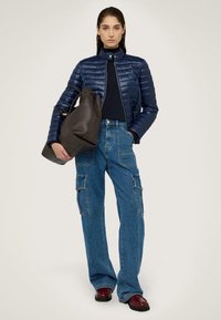 Giacca imbottita navy con trapuntatura orizzontale, abbinata a jeans cargo blu larghi con tasche laterali. Borsa a tracolla in pelle scura.