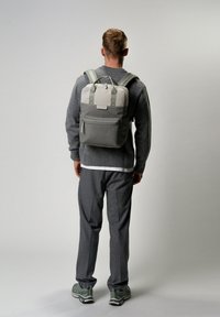 Zaino grigio con maniglia superiore, tasca frontale e spallacci regolabili. Presenta un pannello grigio chiaro nella parte superiore e chiusura con zip.