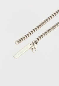 Ezüst lánc nyaklánc összekapcsolt szemekkel, egy "FAVELLA" felirattal gravírozott téglalap alakú címkével és csattal a záráshoz.