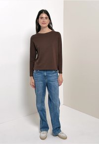 Top à manches longues marron associé à un jean droit bleu clair et des baskets blanches. Design simple, texture lisse et couleurs neutres.