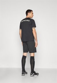 Jersey atlético negro con el texto "Mönchengladbach" en la parte trasera, combinado con pantalones cortos negros y calcetas negras hasta la rodilla. Presenta un diseño simple.