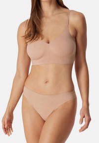 Bralette ja bikinit yhdistelmä sileästä, nude väriisestä kankaasta. Bralette sisältää V-muotoisen pääntien ja ohuita olkaimia; bikinit ovat saumattomalla vyötärönauhalla ja klassisella leikkauksella.