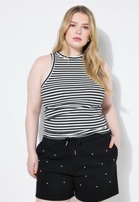 Top senza maniche a righe bianche e nere abbinato a pantaloni corti neri con pois bianchi. Il top ha un colletto alto e un design aderente.