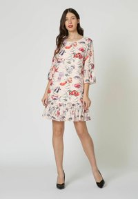 Vestido floral en rosa claro con mangas corta en forma de campana, dobladillo con volantes, patrones en rojo y púrpura vivos, y tejido suave. Llevado con tacones negros.