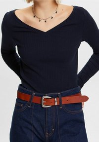 Tummansininen ribattu pitkähiha, jossa V-pääntie, yhdistetty korkeavyötäröisiin farkkuihin ja ruskeaan nahkavyöhön, jossa on hopeinen solki.