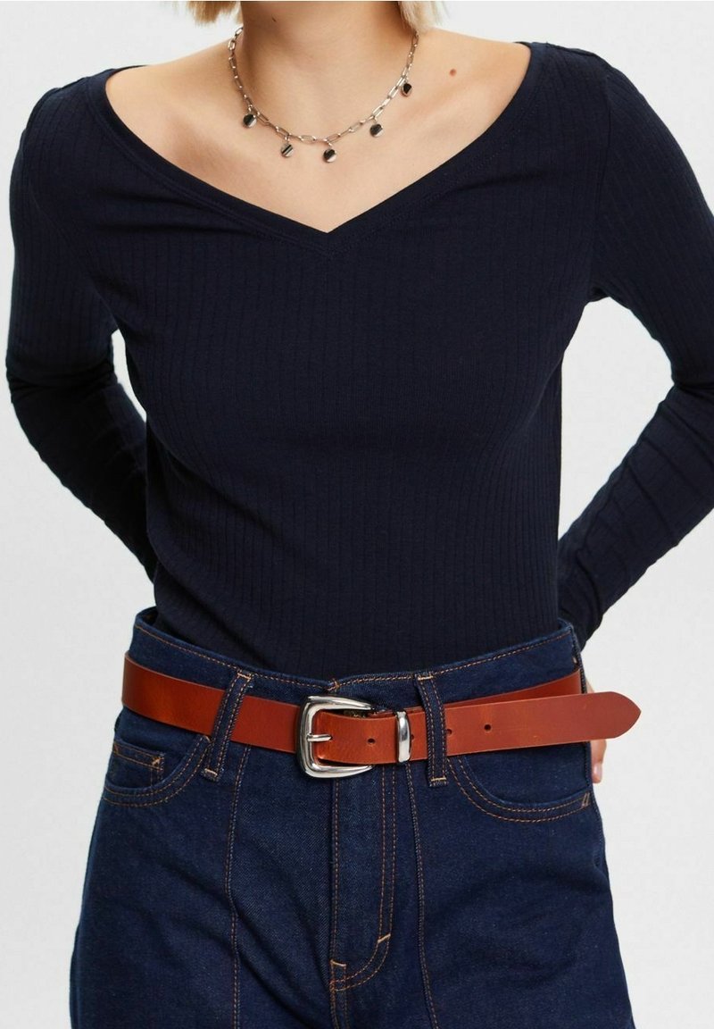 Tummansininen ribattu pitkähiha, jossa V-pääntie, yhdistetty korkeavyötäröisiin farkkuihin ja ruskeaan nahkavyöhön, jossa on hopeinen solki.