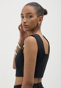 Top corto nero con scollo quadrato, spalline larghe e tessuto testurizzato, caratterizzato da un design semplice e pulito, senza decorazioni.