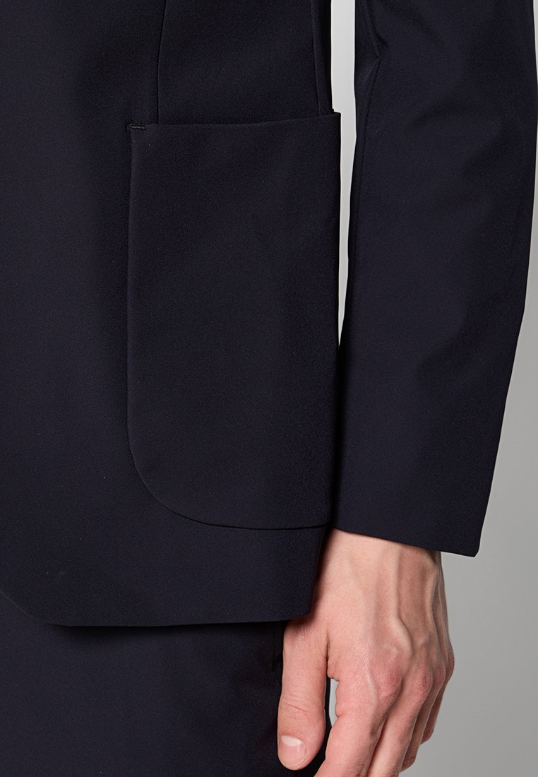 Marineblazer aus einem glatten, strukturierten Stoff mit einer einfachen quadratischen Tasche auf der linken Seite, enganliegendem Design und taillierten Ärmeln.