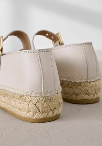 Beiger Leder-Rücken der Espadrille-Schuhe mit geflochtener Jutesohle und goldenen Hardware-Akzenten. Glatte Textur mit genähten Details.