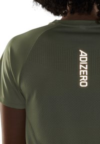 Oliwkowo zielona sportowa koszulka z teksturowanym wzorem, z odblaskowym napisem „ADIZERO” z tyłu dla lepszej widoczności. Krótkie rękawy.