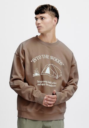 Brun sweatshirt i mjukt material med rund hals, oversized passform och vita tryck av ett tält och en lägereld.