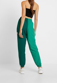 Gröna, lätta joggingsbyxor med elastisk midja och muddar. Har en logodetalj på vänster ben och en slät, strukturerad yta.