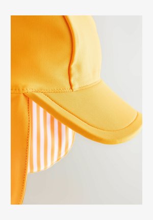 Rumena kapa širokega roba, izdelana iz gladkega blaga. Ima črtasto notranjo podlogo in podaljšan flis na zadnjem delu za zaščito pred soncem.