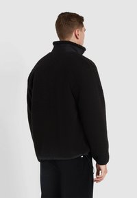 Zwarte fleecejas met hoge kraag, textuur oppervlak en elastische onderrand. Kenmerkt een contrasterende voering en verstelbaar trekkoord in de taille.