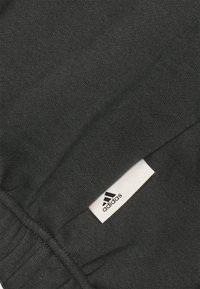 Gros plan sur un tissu noir avec des coutures visibles et une petite étiquette blanche avec le logo Adidas cousue dans la couture.
