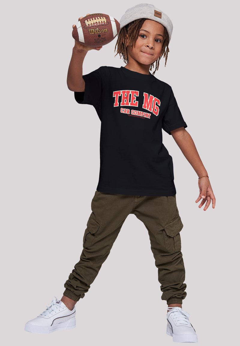 Black t-shirt with "THE MG CAR COMPANY" in red, olive cargo pants, and white sneakers with textured accents. Kid holding a football.