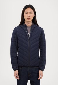 Μπλε επενδυμένη ζακέτα με κουκούλα, με μπροστινό φερμουάρ και σχέδιο σε σχήμα V. Υφασμάτινη επιφάνεια με ελαστικούς ιμάντες και πλαϊνές τσέπες.