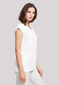 White cotton T-shirt with short rolled sleeves, a V-neckline, and a relaxed fit, displayed on a female model in profile against a neutral background.