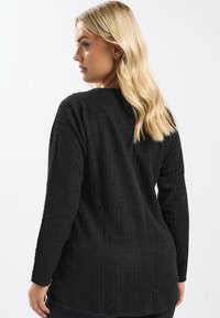 Maglietta nera a maniche lunghe con un tessuto testurizzato che presenta righe verticali, una vestibilità rilassata e un colletto arrotondato. Vista posteriore mostrata.