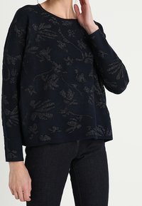 Mörkblå tröja med långa ärmar, prydd med ett texturerat blommönster i en ljusare nyans. Bekväm passform, tillverkad av mjukt material.