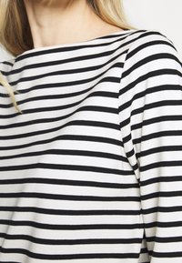 Black and white striped top, featuring a boat neckline, soft fabric, and smooth texture, with an asymmetrical drape on the shoulder.