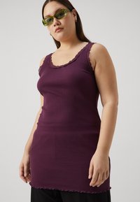 Canotta viola a coste con pizzo sui spallini e sull'orlo, caratterizzata da una silhouette aderente e una consistenza morbida, abbinata a occhiali da sole verdi.