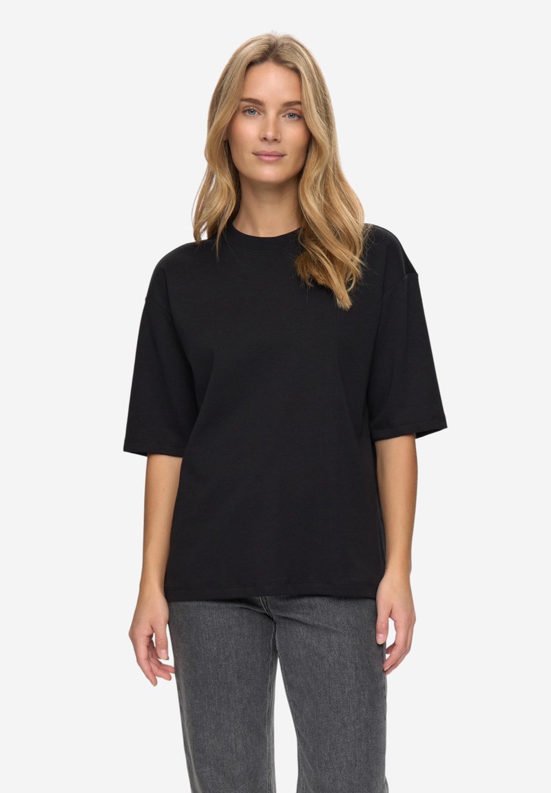 Črna bombažna oversized majica z okrolim izrezom in kratkimi rokavi, kombinirana s temnosivimi jeansa hlačami.