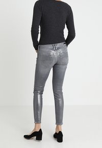 Jeans skinny metálicos plateados con un diseño ajustado. Textura suave, cintura de altura media, dos bolsillos traseros y detalles de costura sutiles.