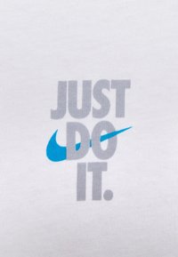 Tejido de algodón blanco con el texto "JUST DO IT" en gris y un acento de swoosh azul de Nike. Tipografía simple y clara sin gráficos adicionales.