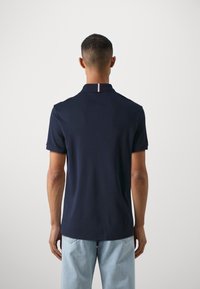 Námořnický polo shirt s krátkými rukávy a plochým límečkem, na zadní straně s červeným a bílým pruhem. Měkký bavlněný materiál, volný střih.