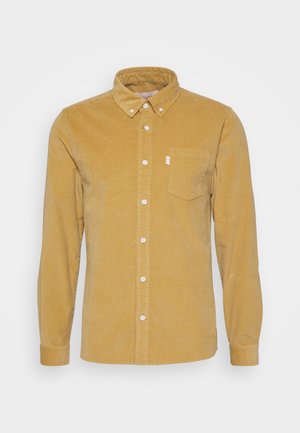 Senfgelbes Cordhemd mit langen Ärmeln, Button-Down-Kragen, weißen Knöpfen und einer Brusttasche auf der linken Seite.