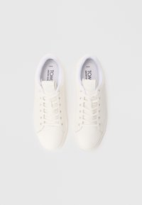 Baskets en toile blanche au texture lisse, avec un design à lacets, des semelles en caoutchouc, et un style minimaliste sans motifs ni accents visibles.
