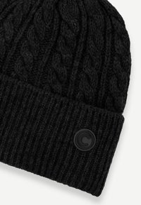 Căciulă neagră tricotată cu un model texturat de cablu, având un manșon ribat și un patch circular negru cu logo pe lateral.