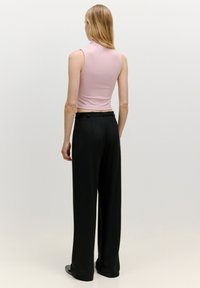 Roze geribbelde mouwloze top gecombineerd met zwarte wijde broek met een hoge taille en strakke lijnen, tegen een neutrale achtergrond.