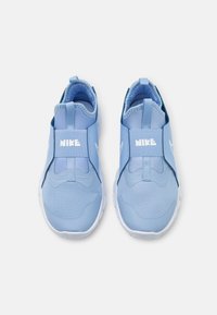 Una coppia di sneakers slip-on Nike di colore blu chiaro con suole bianche e fasce elastiche, viste dall'alto su uno sfondo bianco.