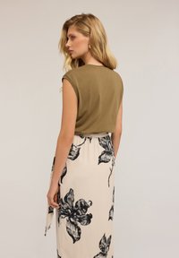 Olivově zelený top s krátkým rukávem v kombinaci s dlouhou krémovou sukní se černými květinovými vzory, hladká látka a upnutý pas.