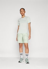 Lys grønn treningsskjorte med korte ermer, kombinert med lys grønne cargo-shorts. Hvite og svarte stripete sokker og grå sneakers.