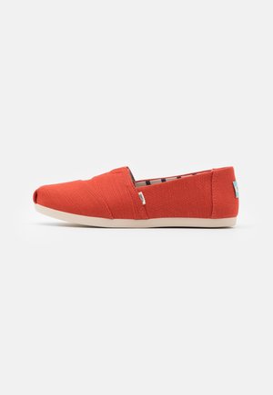 Czerwone płócienne buty typu slip-on z beżową podeszwą, niskoprofilowe, z małymi metkami z tkaniny po bokach i z tyłu, przedstawione w widoku bocznym.